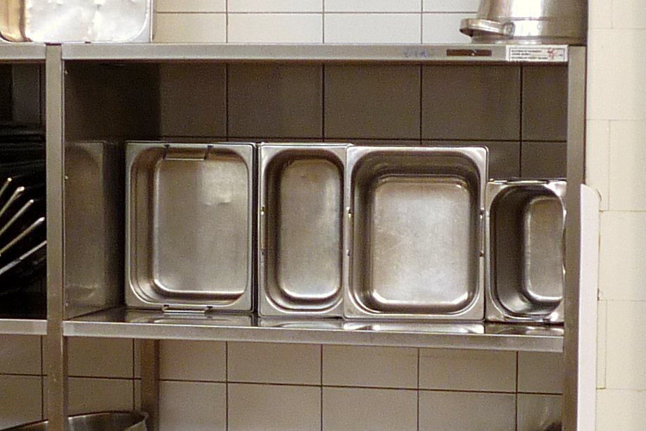Řada nerezových gastronádob na polici výrobní kuchyně